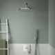 Duschbereich mit einem runden Kopfbrause und einer chromfarbenen Wandarmatur von Ideal Standard. Ein Handbrausehalter und eine weiße Fliesenwand sind ebenfalls sichtbar.